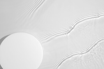 Empty white circle podium on transparent clear calm water texture with splashes and waves in sunlight. Abstract nature background for product presentation. Flat lay cosmetic mockup, copy space.