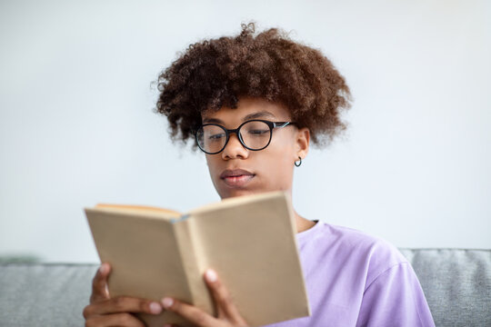 Focused African American Teenager Reading Book, Enjoying Captivating Story At Home