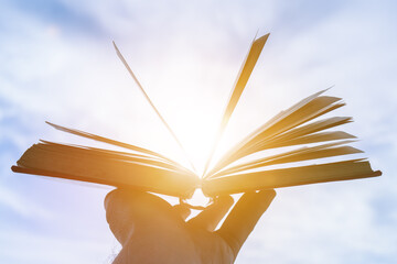 Open book in hand with a glare of the sun on a background of blue sky, reading, learning, knowledge