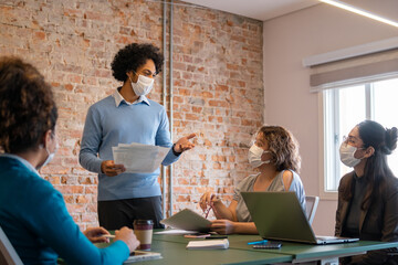 black business man leading presentation for teammates with face mask.