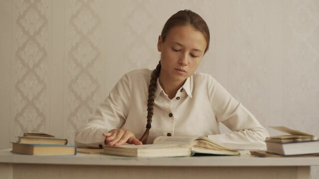 Young woman quickly flips through the book looking for right page. Student sitting at the table at home, preparing for exam, doing homework, looking for information in scientific literature. Education