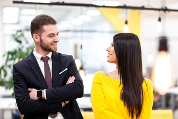 Beautiful Caucasian dark haired girl in yellow posing with businessman wearing suit. Happy colleagues in a modern office.