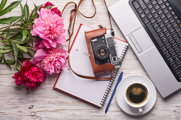 Flat lay women's office desk. Female workspace with laptop, pink peonies bouquet, camera and coffee on white background. Top view feminine background.