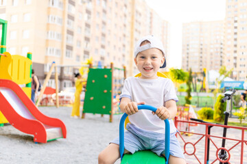 a cheerful child boy swings on a swing in the summer in the yard on the playground or in the kindergarten