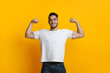Naklejka premium Smiling arab guy showing his biceps on yellow
