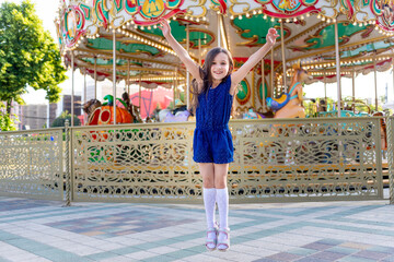 a child girl in an amusement park in the summer jumps with happiness around the carousels and...