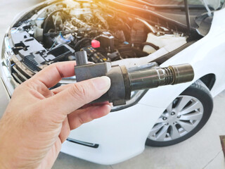 Ignition coil for spark plug of the car ignition system in the mechanic hand with a car blurred...