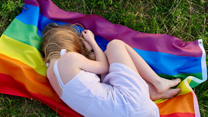 Lesbian woman lying on LGBT flag on grass in white dress. Support of non-traditional orientation in...