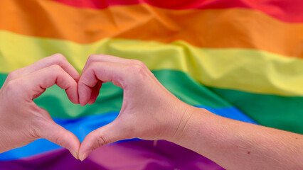 Young lesbian couple holding hands on heart shaped rainbow LGBT flag background. Female homosexual couple celebrates the month of dignity, the day of bisexuality