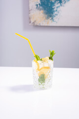 summer drink in a glass glass with lemon, mint and ice on a white table. Minimal summer refreshing concept