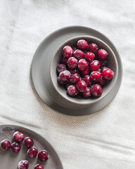 Ripe frozen cherries on grey plate on light textile background, top view