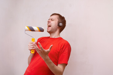 happy Caucasian man singing song using roller brush as a microphone. Young male having fun during...