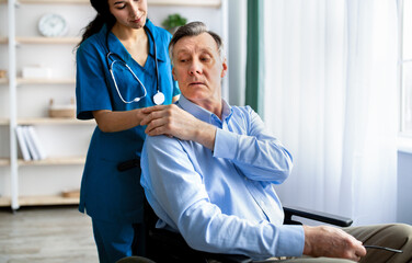 Millennial medical worker holding senior disabled man's hand, supporting him at retirement home