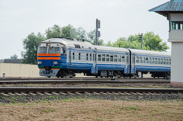 Fototapeta premium An old diesel passenger follows the rails against the backdrop of a morning summer steppe landscape.