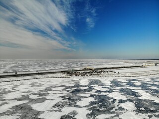 Saint Petersburg Dam at winter in ice. Kronstadt. Snow, and blue sky. A lot cars on parking. A beach covered in snow. High quality photo. Aerial drone view. Flying over.