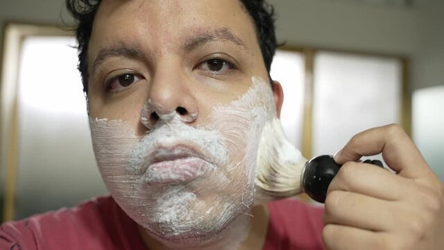 Tired Looking Young Hispanic Man Lathering His Face With Soap Using Old Shaving Brush In The Bathroom