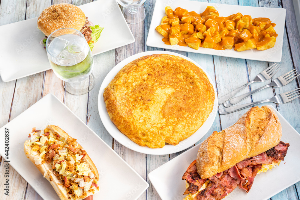 Wall mural Set of Spanish food dishes with potato omelette in the center, patatas bravas, tenderloin sandwich with cheese and hot dog