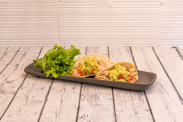 Two Mexican tacos of stewed chicken meat with avocado guacamole, lettuce and chunks of tomato with onion