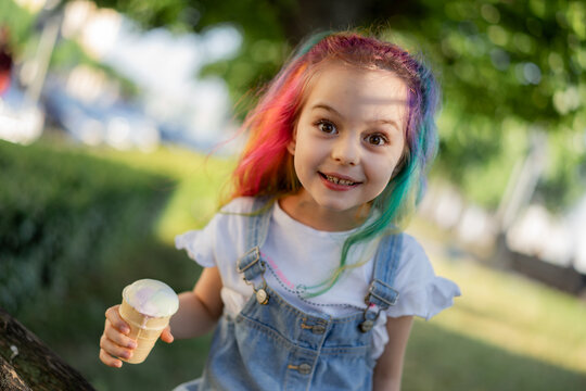 Happy little girl with colorful dyed hair eating ice cream outdoors in park. Image with selective focus