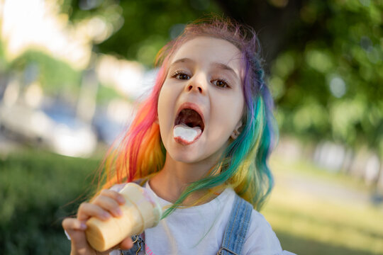 Happy little girl with colorful dyed hair eating ice cream outdoors in park. Image with selective focus