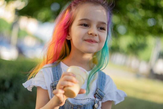 Happy little girl with colorful dyed hair eating ice cream outdoors in park. Image with selective focus