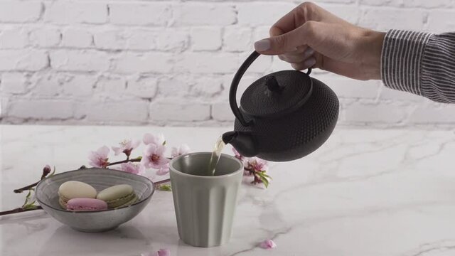 Hand pouring a glass of tea with flowers and macaroons in the background. Cinemagraph concept.