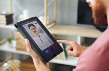 Closeup of young guy looking at photo of pretty woman on tablet display. Close up of man presses red heart like button and sends message to beautiful girl on modern online dating website or mobile app