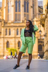 Lifestyle of a young girl of black African ethnicity with a beautiful green suit. Sightseeing in the city walking next to a cathedral