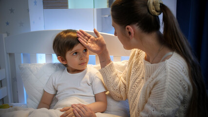 Young mother touching and kissing her little son with hight temperature in forehead. Concept of...