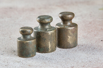 Three antique bronze weights for scales on concrete background.