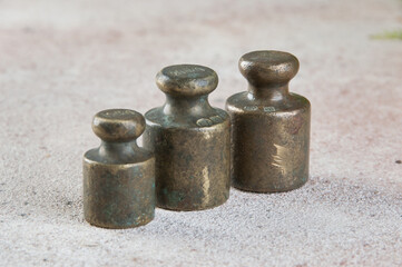 Three antique bronze weights for scales on concrete background.