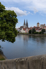 Blick von der Wöhrd auf Dom, steinerne Brücke , Rathausturm und Ufer  mit Wolken am Himmel und Bäumen im Vordergrund