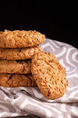 A stack of oatmeal cookies on a kitchen napkin on a wooden table against the dark background