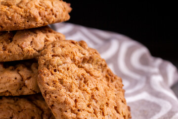 A stack of oatmeal cookies on a kitchen napkin on a wooden table against the dark background