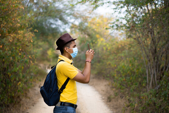 Latino tourist with yellow clothes and blue mask, taking photo with his cell phone. Hispanic man using mobile technology. Traveler with mask and blue backpack. Horizontal image.