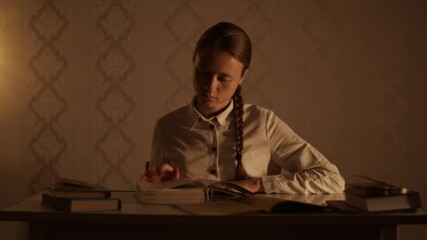 Young woman sitting at the table with books in the evening, open and flipping pages of  encyclopedia book. Education, studying at home, library, do homework, prepare for examination. Student lifestyle