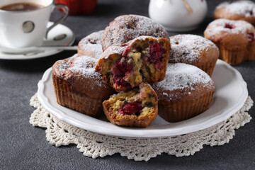 Muffins with cherries sprinkled with powdered sugar on a white plate on a dark background.