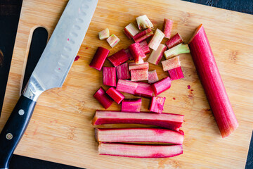 Fototapeta na wymiar Chopped Rhubarb Stalks on a Bamboo Cutting Board: Chopping rhubarb with a Santoku chef's knife