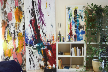 Abstract art paintings on wall of stylish modern living room interior with bookcase, home plants and paints