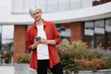 Smart confident teenager with his phone outside. Portrait of blonde young hipster with his phone.