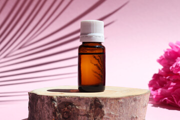 Bottle of essential oil on a wood cut with peony flowers and palm leaf shadow. Natural or...