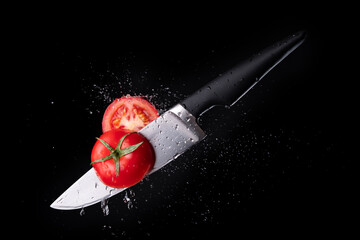 Fresh ripe tomato cutting with a knife and flying in motion on the black background with red splashes - obrazy, fototapety, plakaty