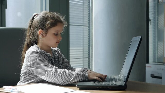 Adorable preschool child working on a laptop at the table. Cute little girl in formal clothes sitting in office and workplace