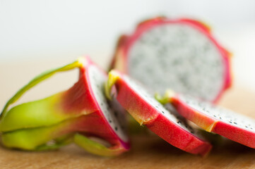 Slices of dragon fruit or pitaya with pink skin and white pulp with black seeds on wooden cut board...