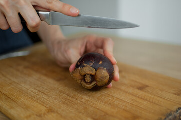 Female hands is cutting with knife a fresh ripe mangosteen on a cut wooden board. Exotic fruits, healthy eating concept