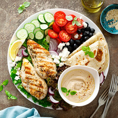 Chicken breast grilled with fresh vegetables, olives, feta cheese, flatbread and hummus, top view