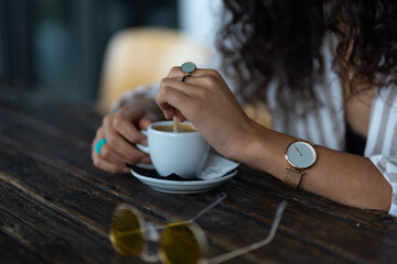 woman with rings and watch having a cup of coffee at wooden table