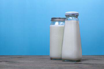 Two different glass milk bottles, on a wooden table on a blue background.