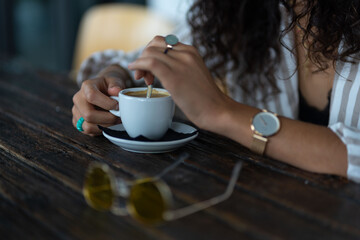 woman with rings and watch having a cup of coffee at wooden table