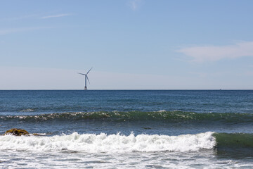 A wind turbine out on the ocean with gentle waves in front